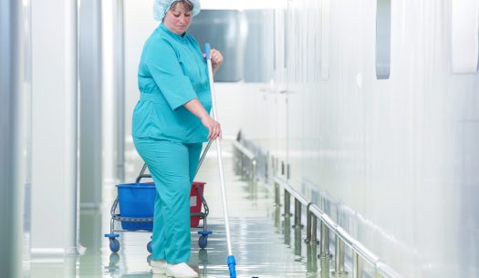 Adult cleaner maid woman with mop and uniform cleaning corridor pass floor of pharmacy industry factory or clinic