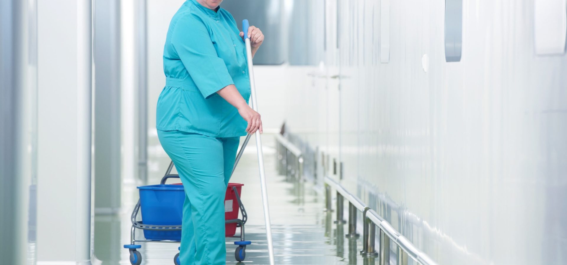 Adult cleaner maid woman with mop and uniform cleaning corridor pass floor of pharmacy industry factory or clinic